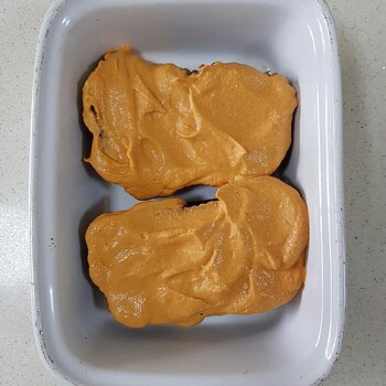 Tempeh loaf slices coated in a creamy tomato sauce before baking