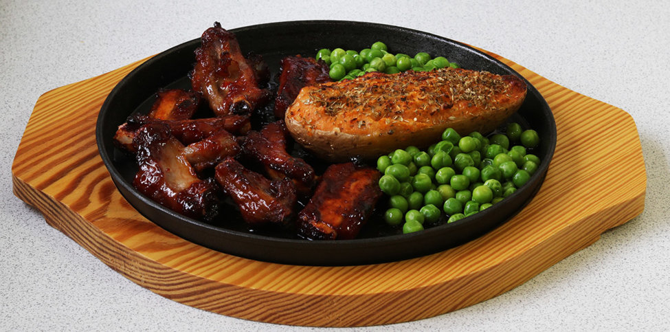 Honey glazed pork ribs with stuffed jacket potato and peas.