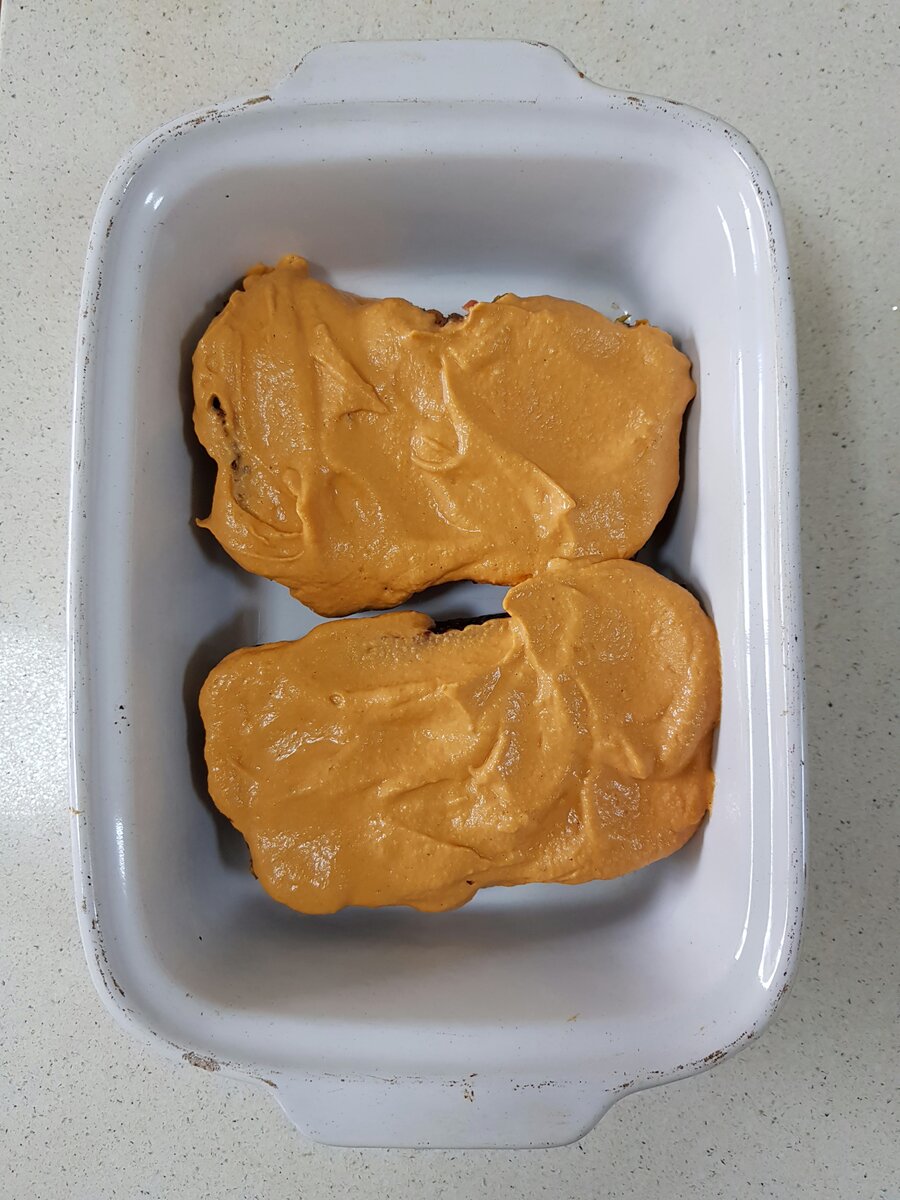 Tempeh loaf slices coated in a creamy tomato sauce before baking